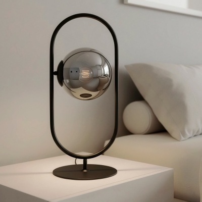 Candeeiro de mesa moderno preto com bola de vidro espeçado sobre mesa de cabeceira branca, cama com almofadas brancas ao lado