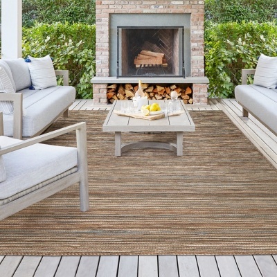 Conjunto de móveis de jardim com sofá, cadeira, tapete riscado bege e castanho, e lareira de tijolo com lenha