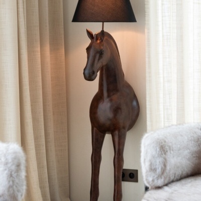 Luminária de cavalo castanho com abajur preto numa sala com cortinas bege e sofás peludos cinza