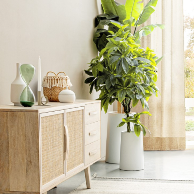 Aparador de madeira clara com decoração e plantas grandes em vasos brancos numa sala clara