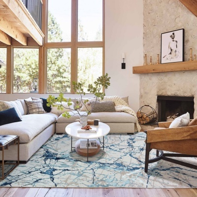 Sala de estar com sofá bege, mesa de centro redonda, tapete azul e branco, poltrona castanha e lareira de pedra