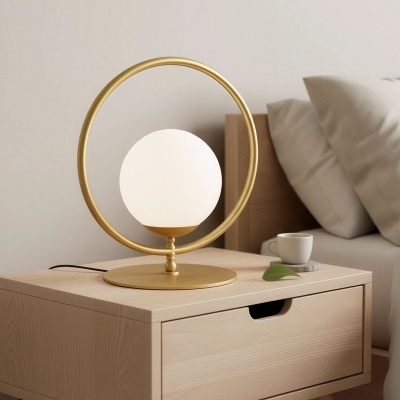 Candeeiro de mesa dourado com cúpula branca numa mesa de cabeceira de madeira clara