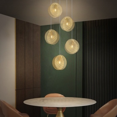 Lustre pendente dourado com cinco luminárias redondas texturizadas numa sala com mesa redonda e cadeiras castanhas