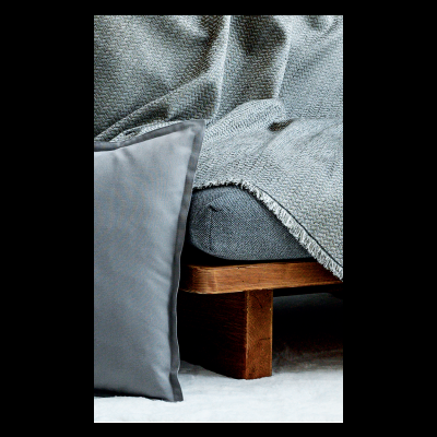 Sofá cinza com estrutura de madeira, cobertor cinza texturizado e almofada cinza lisa