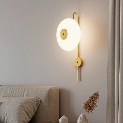 Abajur de parede branco redondo com detalhes dourados junto a cama e criado-mudo com vasos