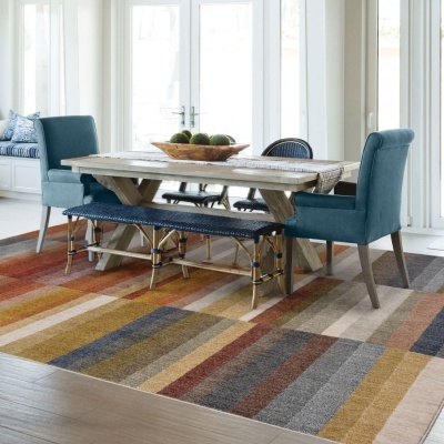Mesa de jantar em madeira com bancos e cadeiras azuis sobre tapete colorido de riscas