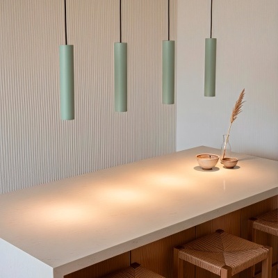 Bancada clara com quatro banquetas de madeira e quatro candeeiros verdes pendentes.