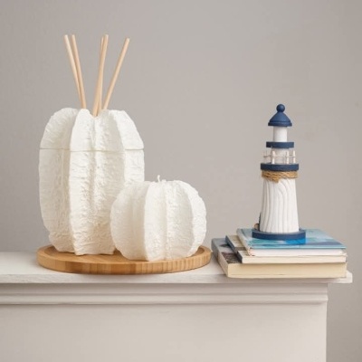 Difusor de aromas e vela decorativa brancos, farol azul e branco e livros sobre prateleira.