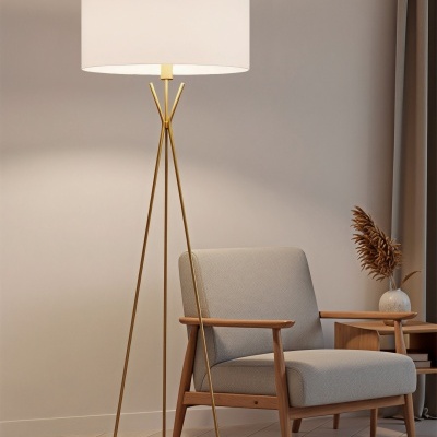 Candeeiro de pé dourado com abajur branco ao lado de poltrona bege e mesa de madeira