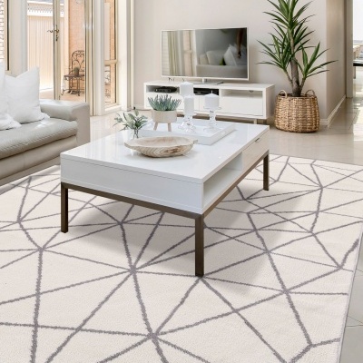 Sala de estar com mesa de centro branca, tapete bege com padrão geométrico, e sofá claro