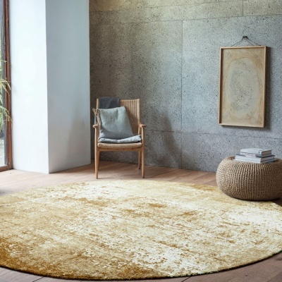 Tapete redondo dourado com cadeira de madeira e pufe trançado em sala com parede cinzenta