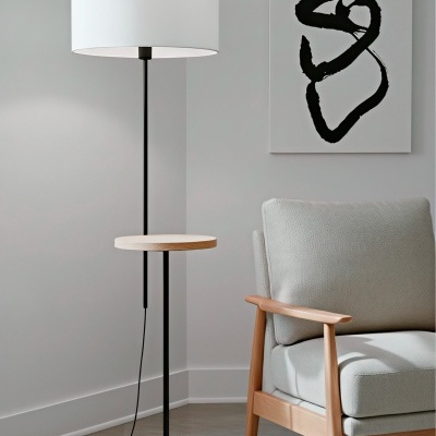 Lâmpada de pé preta com cúpula branca e mesa de apoio em madeira clara ao lado de poltrona cinza clara com estrutura em madeira.