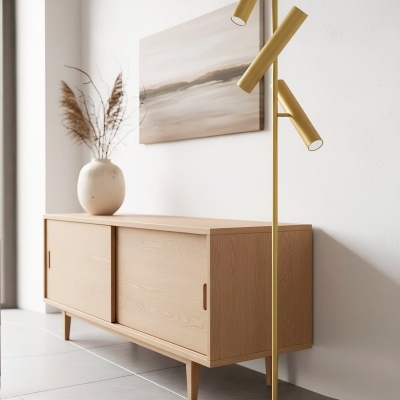 Candeeiro de pé dourado com três focos, móvel de madeira clara com portas deslizantes, vaso cerâmico com ramos secos, quadro abstrato em tons bege