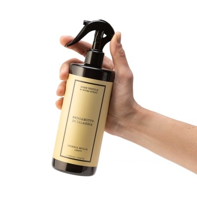 Frasco negro com spray e etiqueta bege com texto, segurado por mão