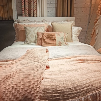 Cama decorada com edredão rosa salmão e almofadas decorativas em tons de creme e rosa