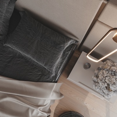 Vista aérea de cama com cabeceira bege, roupa de cama preta, manta cinza, mesa de cabeceira com flor branca e candeeiro, almofada redonda preta no chão de madeira