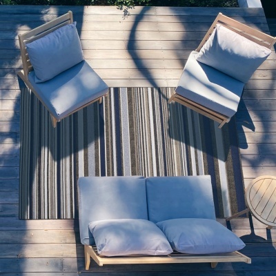 Conjunto de móveis de exterior com almofadas brancas, tapete riscado e chão de madeira