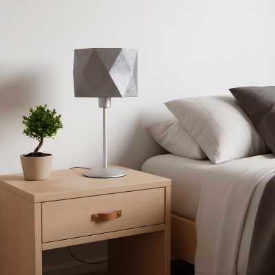 Mesa de cabeceira em madeira clara com candeeiro e planta ao lado de cama com roupa branca e cinza