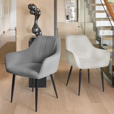 Duas cadeiras estofadas modernas, cinzenta e branca, com pernas pretas finas, em ambiente interior com chão de madeira e escada de vidro