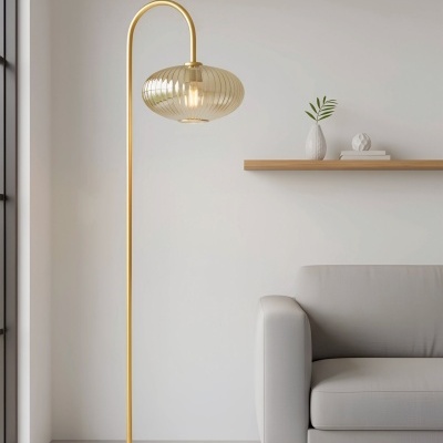 Candeeiro de pé dourado com cúpula de vidro ao lado de sofá cinzento e prateleira de madeira