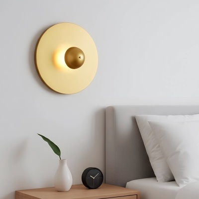 Mesa de cabeceira com jarro, relógio preto, cama cinzenta e candeeiro de parede dourado