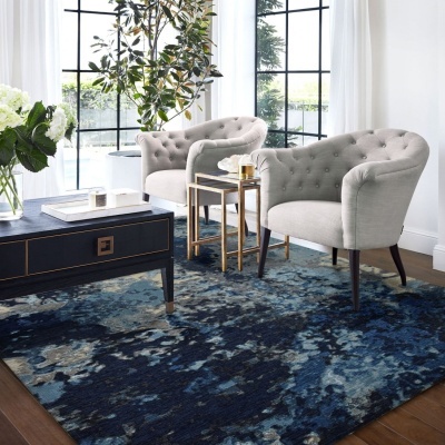 Sala de estar com poltronas cinza, mesas e tapete azul