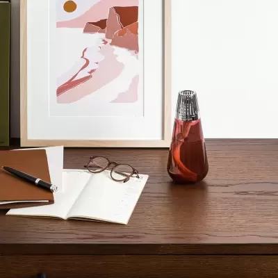 Mesa de madeira com frasco de vidro, óculos, cadernos e arte abstrata na parede