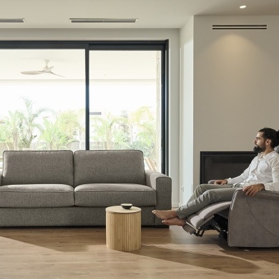 Sala de estar com sofá cinzento, poltrona reclinável, mesa baixa e porta de vidro grande.