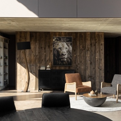 Sala de estar com parede de madeira rústica, duas poltronas, mesa redonda e quadro de leão