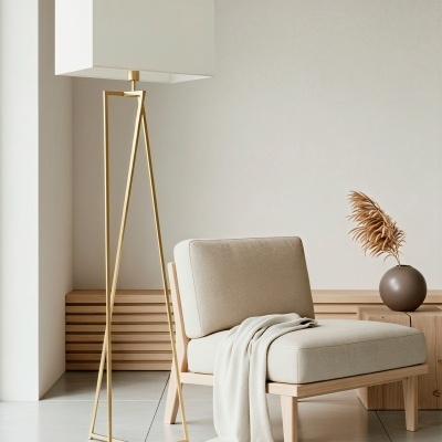 Luminária dourada com abat-jour branco e cadeira bege com manta em sala minimalista