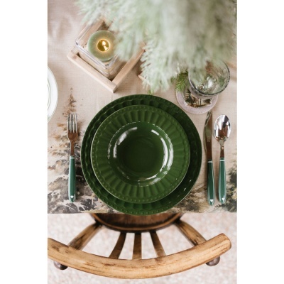 Conjunto de loiça verde e talheres sobre toalha estampada e cadeira de madeira