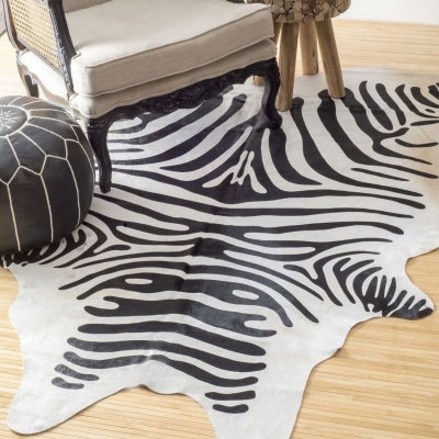 Tapete com padrão de zebra preto e branco junto a poltrona, otoman e mesa de madeira.