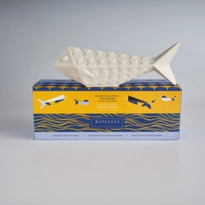 Figura decorativa branca em forma de peixe sobre caixa azul e amarela com peixes e texto SANULENA