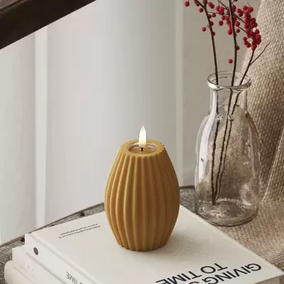 Vela amarela com textura ondulada acesa sobre livros e frasco de vidro com ramos vermelhos