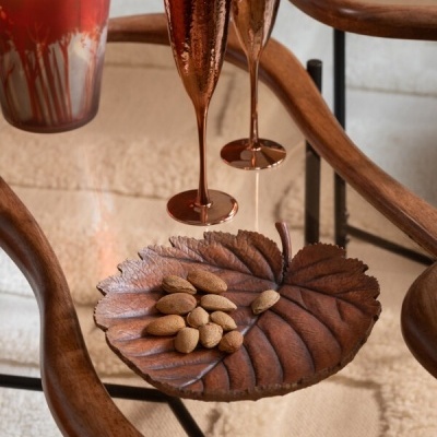 Prato decorativo em folha com amêndoas, taças cobre e vela vermelha sobre mesa de vidro e madeira