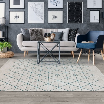 Sala de estar com sofá bege, cadeira azul, mesa metálica, tapete bege geométrico e quadros na parede cinza