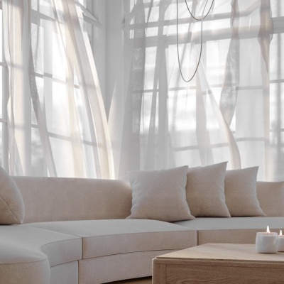 Sofá curvo bege com mesa baixa de madeira e luminárias brancas pendentes numa sala luminosa com cortinas translúcidas