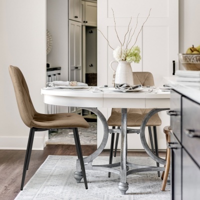 Mesa de jantar redonda branca com cadeiras castanhas estofadas e jarro decorativo com flores