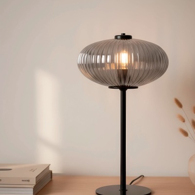 Candeeiro de secretária com abajur em vidro cinza e base preta numa mesa de madeira clara