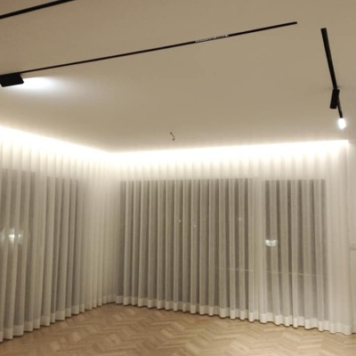 Sala com cortinas brancas translúcidas, chão de madeira e teto com iluminação moderna