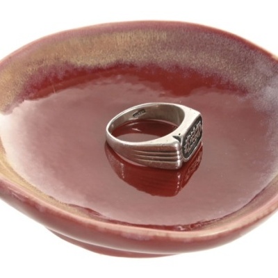 Anel prateado com pedra escura numa tigela de cerâmica vermelha
