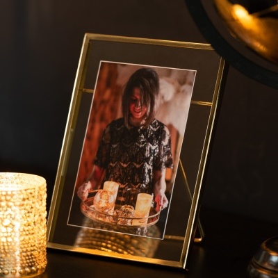 Moldura de foto dourada com foto de mulher segurando bandeja com velas e vela votiva dourada ao lado.