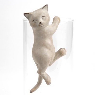 Escultura de gato bege pendurado na borda de um copo de vidro