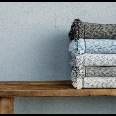 Pilhas de toalhas ou mantas em tons cinza e azul sobre banco de madeira
