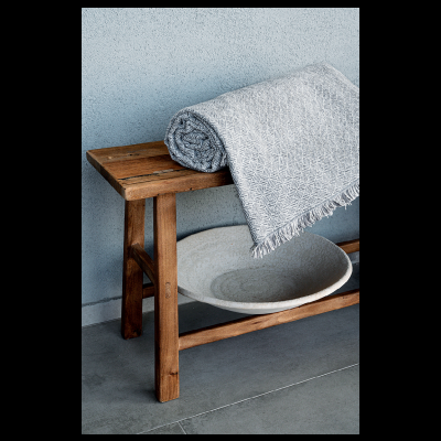 Cobertor cinzento com padrão geométrico sobre banco de madeira rústico