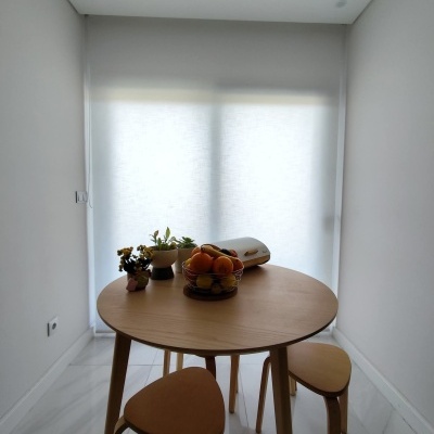 Mesa de jantar redonda de madeira com bancos, frutas e plantas numa sala branca