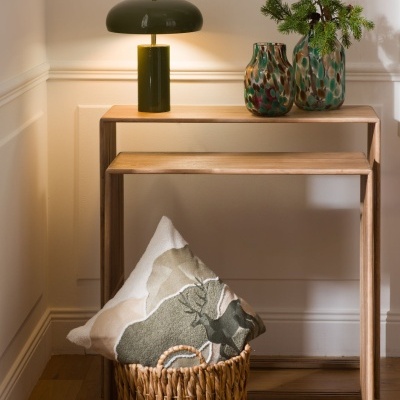 Móvel de madeira com candeeiro verde, dois vasos cerâmicos e cesta de vime com almofada decorativa.