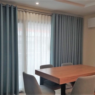 Sala de jantar com mesa de madeira e cadeiras cinza, cortinas azuis e ar condicionado na parede.