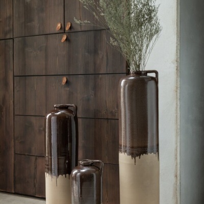 Três vasos altos de cerâmica bicolor com textura brilhante e alça, em ambiente com armário de madeira escura.