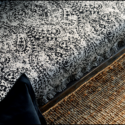 Cobre-cama em padrão preto e branco com franjas junto a almofada preta e tapete de fibras naturais